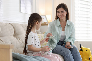 Mother giving pocket money to her daughter on sofa at home