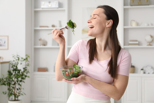 Woman in fitness clothes eating salad at home, space for text. Healthy food