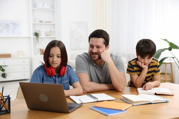 Father helping his kids with homework at wooden table indoors