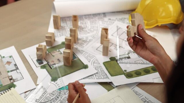 Architect and engineer consider or discuss about building construction using blueprint on table with architectural document, measurement tool and wooden block scatter around at office. Delineation.