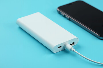 A close-up of a sleek and modern slim power bank placed next to a phone charging cable, both on a bright blue background.