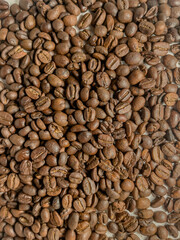 Top view of roasted coffee beans scattered across a white surface showing rich texture and natural brown color tones. 