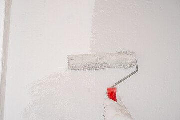 A woman manually paints a wall with a paint roller. Painting the apartment