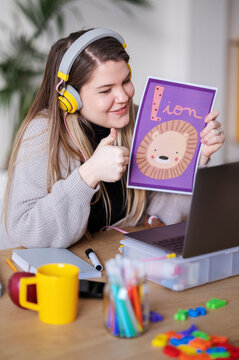 A teacher is giving a thumbs up while teaching the word "lion" during an online class. She's using visual aids to help her students learn.