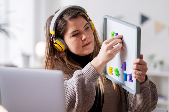 A woman uses a whiteboard with magnetic letters. She's likely teaching remotely, using the letters as a visual aid for her students.