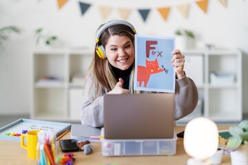 A teacher is leading a virtual lesson, showing a picture of a fox to help kids learn the alphabet. She's using a laptop to connect with her students.