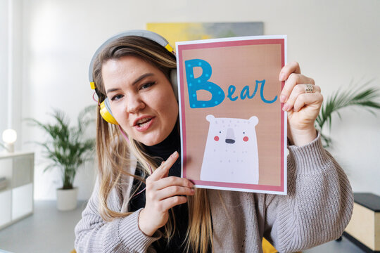 A teacher is showing a flashcard with the word "Bear" and a bear illustration. She's teaching young children how to read and identify animals.