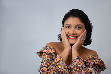 Smiling woman with hands on face wearing floral blouse. Ideal for skincare, beauty, fashion, self-care, or wellness advertisement campaigns. Studio portrait with copy space.