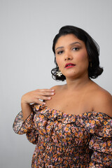 Charming brunette woman with confident expression, hand on shoulder. Ideal for fashion, empowerment, authenticity, beauty, self-expression. Studio shot with copy space on gray background.