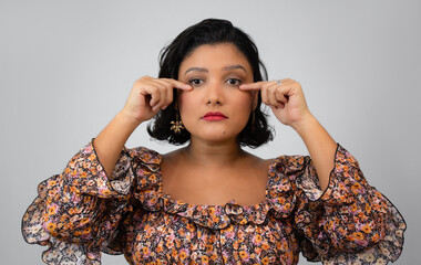 Horizontal portrait of beautiful woman pointing to her eyes. Suitable for ophthalmology, tears, vision, sadness, personal care and emotional health. Copy space on gray background.