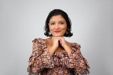 Charming, confident woman, chin on hands, smiling at the camera. Ideal for beauty, female empowerment, fashion and femininity. Horizontal studio portrait with copy space on gray background.