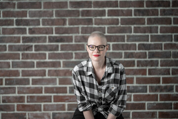 Obraz premium Portrait of a beautiful young caucasian woman with shaved head. Female cancer survivor. Smiling Woman with Glasses Posing Confidently in a Studio Environment. Model Has Glaucoma. Waering Plaid Shirt