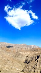 Cloud floats above rugged range while cloud shadows fall below, cloud formation contrasts rocky stillness, sky movement, and wide atmospheric presence across desert mountain terrain.