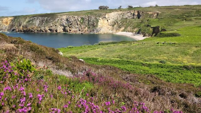 Aerial view of the rocky coastline at Pointe de Pen-Hir on the Crozon Peninsula, Brittany, France. Steep cliffs, azure ocean water, and a clear blue sky. Birdsong can be heard in the background.