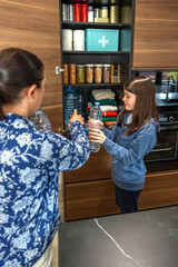 Family preparing 72 hour survival kit for war or natural disasters. Mother and daughter storing water bottles, food and supplies in kitchen pantry. Alert, foresight and self sufficiency strategy.