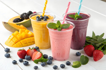 Three colorful fruit smoothies in plastic cups garnished with fresh berries and mint a healthy and refreshing beverage concept