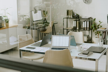 Contemporary office environment featuring open plan workstations with laptops and documents placed on desks under natural lighting conditions