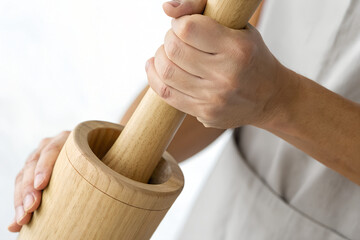 Hands grinding with a wooden mortar and pestle.