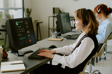 Woman with headset working on computer in modern office environment with other colleagues in...
