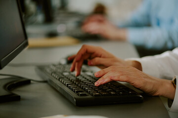 Focused hands on keyboard in modern office setting, with blurred background and technology present. Fingers actively engaged in typing