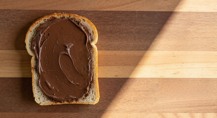 Slice of bread topped with chocolate spread on wooden surface  