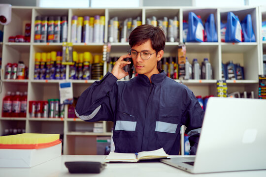 Mechanic managing orders in auto parts store using laptop and phone