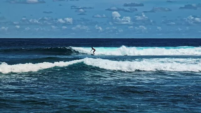 Profile view of a lone surfer rideing turquoise water of ocean under partially cloudy sky in Nyang Nyang Beach of Bali, Indonesia.