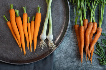 Fresh raw peeled and unpeeled carrots lie on a table. Cleaned onions lie next to them. A large tray...