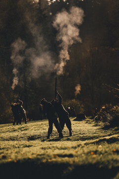 A vertical photograph of Silhouettes of guns shooting with gun smoke on a pheasant shoot in UK