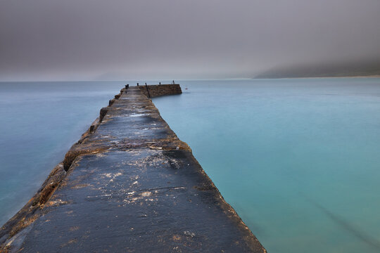 A misty, murky dawn view of the breakwater at Sennen Cove; on the Atlantic coast near Land's End, in the far west of Cornwall, United Kingdom