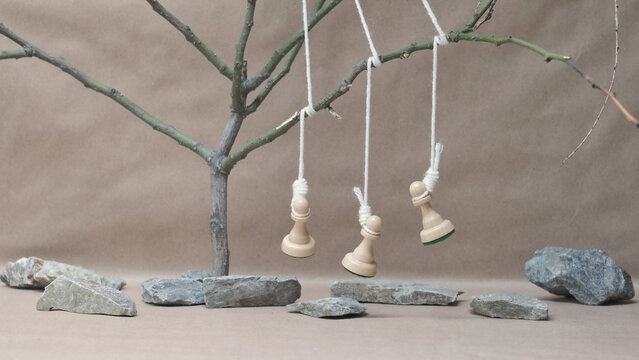 three chess pieces white pawns hanging on a noose among stones