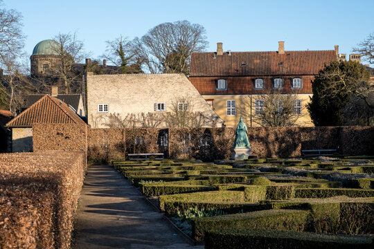 View of Kongens Have with tree-lined paths and blooming gardens, featuring Queen Caroline Amalie's statue subtly in the distance, blending nature with royal remembrance.