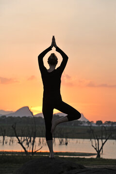 Young woman practising yoga posture by the Senanayake Samudraya Lake at sunset, Gal Oya National Park, Sri Lanka, Indian subcontinent, South Asia