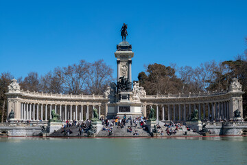 People relaxing in front of the Monument to Alfonso XII and boating lake in Retiro Park in the heart of the capital city of Madrid, Spain
