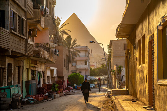 View of Giza Pyramid and local woman in Cairo backstreet during golden hour, Cairo, Egypt, Africa