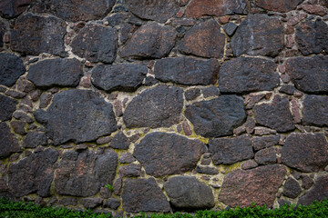 A wall of large granite stones with a green strip of grass growing at the bottom