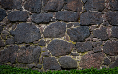 A wall of large granite stones with a green strip of grass growing at the bottom
