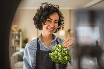 curly hair woman use cellphone for live stream and present home plant