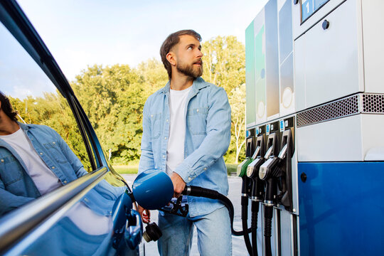 Handsome bearded European man refueling his car and looking on scoreboard, standing on self service petrol station
