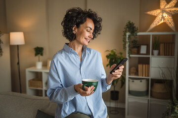 curly hair mature woman use mobile phone and drink coffee at home