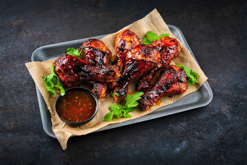 Authentical barbecue chicken drumsticks with hot chili sauce as marinade and coriander leaves served as close-up on a backing sheet a paper