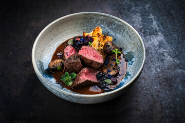 Barbecue dry aged venison steaks - deer entrecote cut english roasted served with grilled mushrooms, fruit berry gravy sauce and panettone herbs served as close-up on a design plate