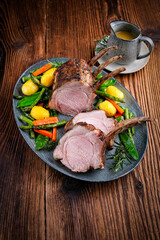 Juicy dry aged bone-in back rack of pork loin roast served as close-up with herbs and vegetable mix...