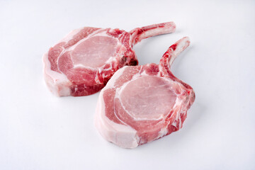 Raw dry aged trimmed bone-in pork loin chops cutlets offered as close-up on white background -...