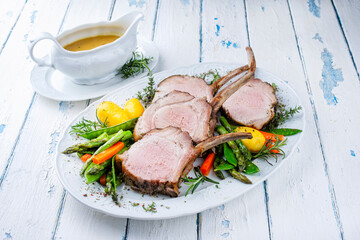 Juicy dry aged bone-in back rack of pork loin roast with dressing sauce served as top view with herbs and vegetable mix on a Nordic design plate