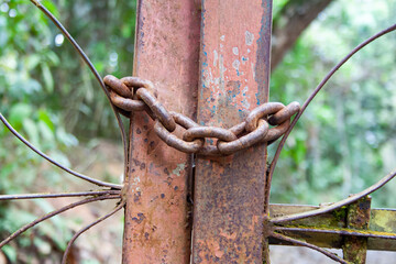 Close-up detail of corroded fence with chain in mountainous jungle.