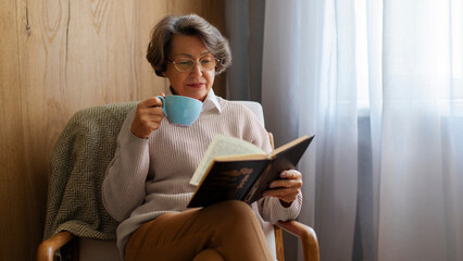 Senior woman relaxing, reading book and drinking coffee at home, enjoying quiet time and leisure...