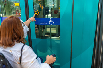 Woman in wheelchair entering public transport using accessible button