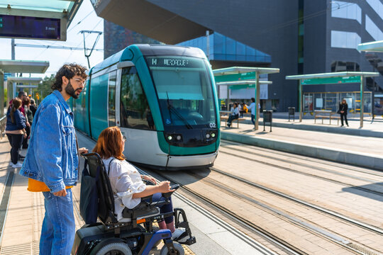 Young man assisting woman in wheelchair waiting for tram at station