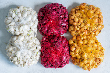 Three varieties of onion sets, yellow, white and purple, in mesh bags on a table, showing the variety of varieties ideal for spring planting and home gardening,